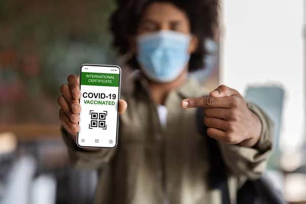 Black Guy Pointing At Smartphone With Digital Covid-19 Vaccination Certificate On Screen