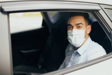 Orta Doğulu koruyucu maskeli bir adam takside oturuyor.