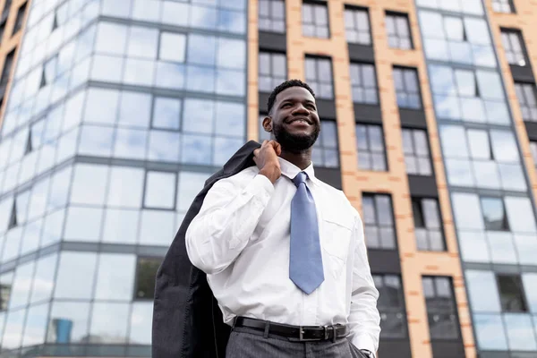 Glad afrikansk amerikansk affärsman håller jacka på axeln och lämnar modernt kontor byggnad — Stockfoto