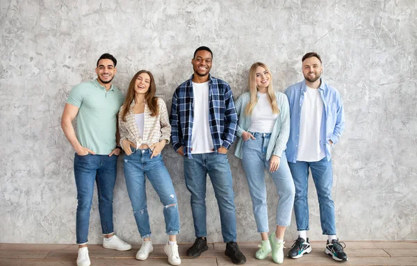 Longitud completa de amigos interracial sonriendo y mirando a la cámara, posando contra la pared gris del estudio —  Fotos de Stock