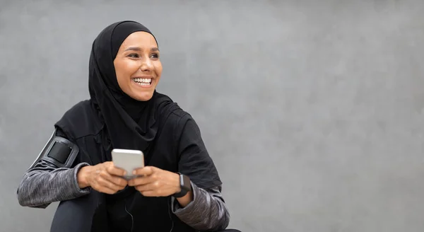 Atletik muslim wanita dalam pakaian olahraga sederhana santai dengan smartphone setelah pelatihan di luar ruangan — Stok Foto