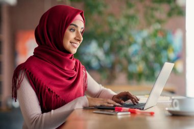 Dini Müslüman kadın dizüstü bilgisayarda, klavyede, kafenin içinde daktilo kullanıyor.