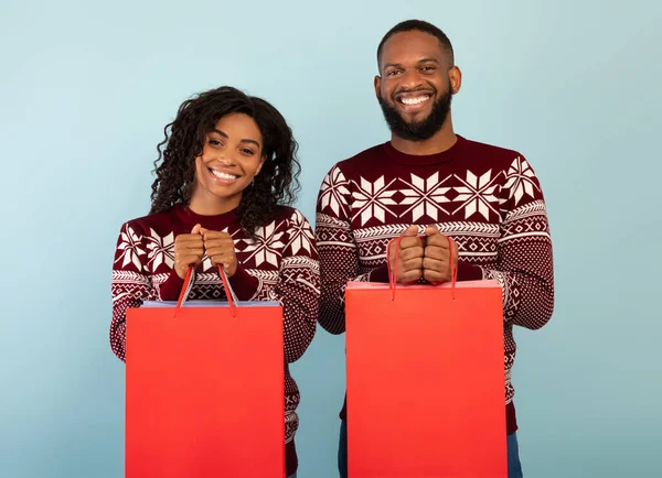 Happy african american pasangan memegang tas belanja dengan hadiah Natal atas latar belakang biru, ruang untuk desain — Stok Foto