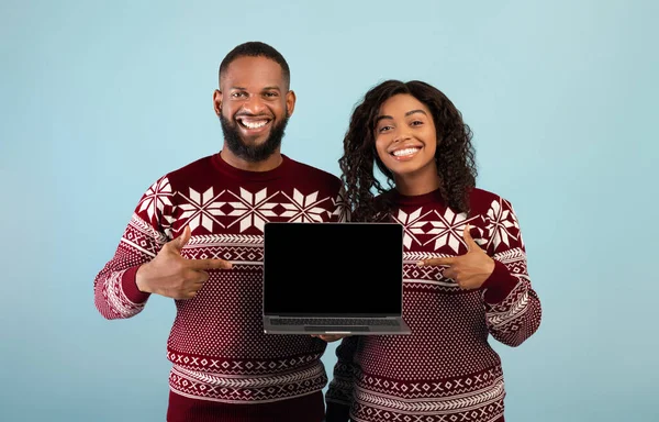 Compras online de Natal. Feliz casal afro-americano mostrando laptop com tela vazia, apontando sobre ele — Fotografia de Stock