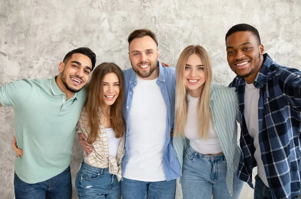 Retrato de amigos inter-raciais alegres posando para a câmera, sorrindo, passando tempo juntos contra a parede do estúdio cinza — Fotografia de Stock