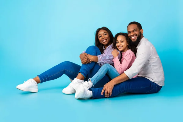 Zwarte man knuffelen glimlachende vrouw en dochter, zitten op de vloer — Stockfoto