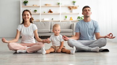 Üç kişilik mutlu bir aile ve bebek evde birlikte meditasyon yapıyorlar.