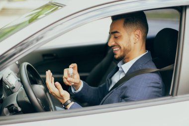 Neşeli iş adamı arabada otururken dezenfektan spreyi kullanıyor.