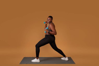 Tombul siyah, yoga minderinde halterlerle egzersiz yapıyor.