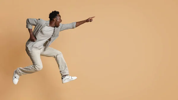 Crazy Sales. Emotional black man pointing aside while jumping over beige background