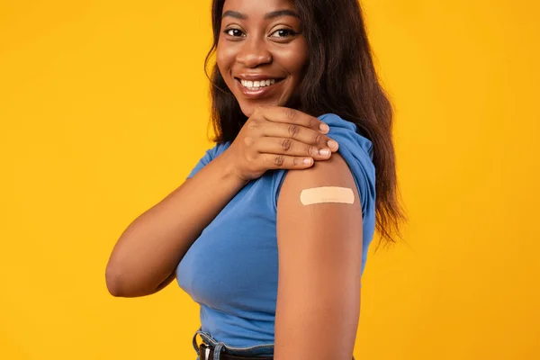 Dama afroamericana mostrando brazo vacunado, fondo del estudio amarillo, recortado —  Fotos de Stock