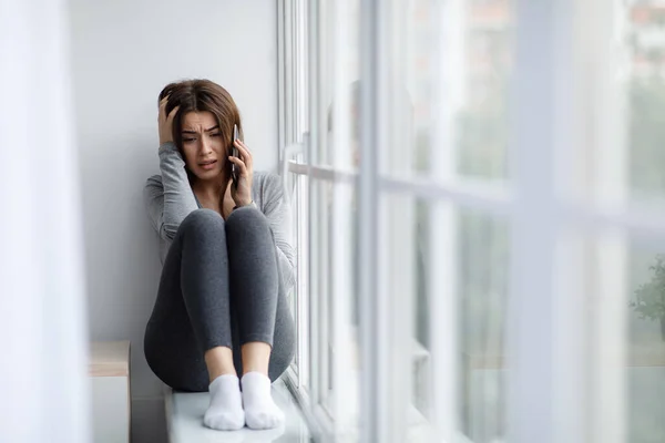 Плач засмучена стурбована біла молода жінка, що страждає від депресії та комунікаційних проблем, розмовляє по телефону — стокове фото