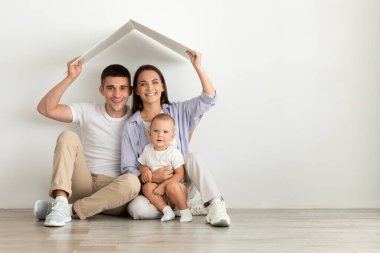 Aile Konutları. Karton çatının altında oturan şirin bebekli mutlu ebeveynler.