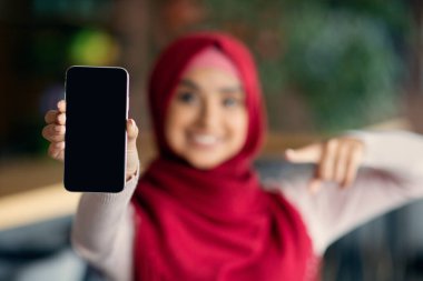 Tanımlanamayan tesettürlü kadın cep telefonunu boş ekranla gösteriyor.