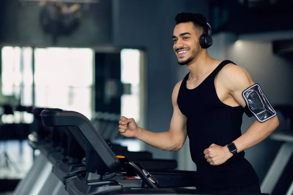 Bonito homem árabe muscular em fones de ouvido sem fio Jogging na esteira no ginásio — Fotografia de Stock