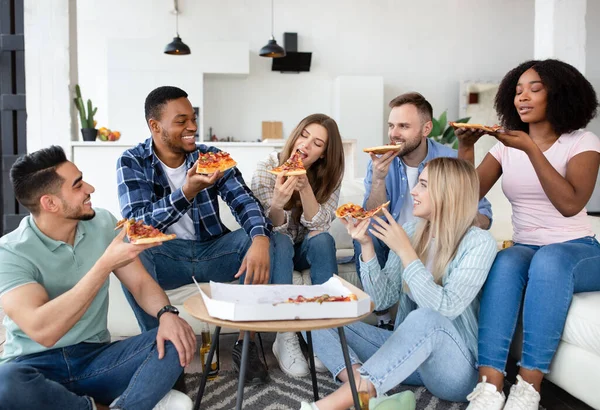 Amici multirazziali spensierati che fanno festa in casa, mangiano pizza, chiacchierano e ridono, passano del tempo a casa — Foto Stock