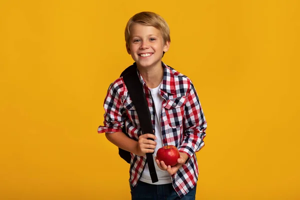 Positivo europeo adolescente alumno con mochila sosteniendo manzana roja, compartir y mirar a la cámara — Foto de Stock