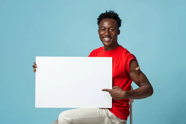 Informationen zur Impfung. Lächelnder afroamerikanischer Typ mit Gips auf dem Arm, der ein leeres Plakat hält — Stockfoto