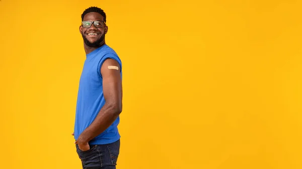 Schwarzer Mann zeigt geimpften Arm nach Schuss auf gelbem Hintergrund — Stockfoto