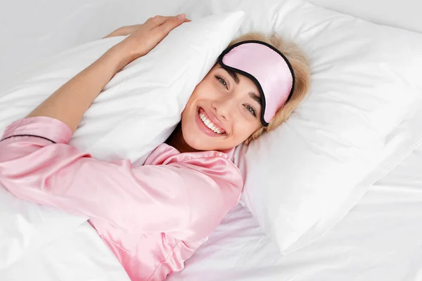 Αστεία ευτυχισμένη νεαρή ευρωπαϊκή ξανθιά κυρία σε ροζ πιτζάμα, μάσκα ύπνου, αγκαλιές με μαξιλάρι — Φωτογραφία Αρχείου