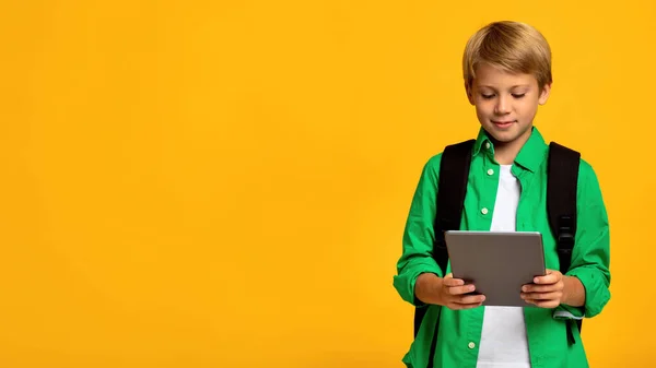 Uśmiechnięty biały nastolatek chłopiec student z plecak wpisując na tablet i oglądając edukacyjne wideo — Zdjęcie stockowe