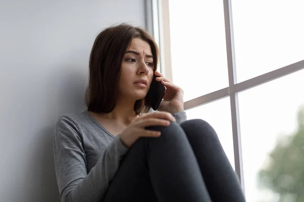 Невдача шокована пригніченою молодою досить кавказькою жінкою, яка телефонує, отримала погані новини або розпадається біля вікна — стокове фото