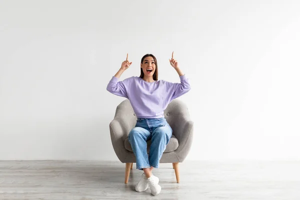 Opgewonden blanke vrouw met idee en wijzen twee vingers omhoog naar kopieerruimte, zitten in de fauteuil, mockup — Stockfoto