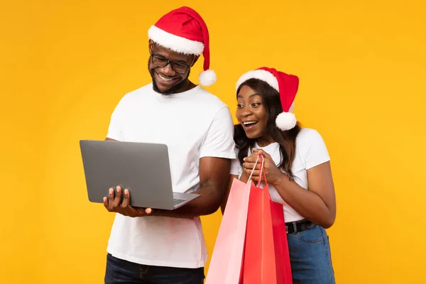 Μαύρο ζευγάρι που αγοράζουν χριστουγεννιάτικα δώρα σε απευθείας σύνδεση με το φορητό υπολογιστή, κίτρινο φόντο — Φωτογραφία Αρχείου