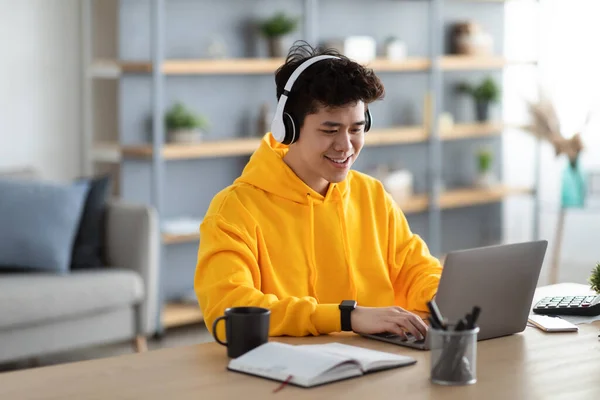 Sorridente uomo asiatico in auricolare lavorando su laptop a casa — Foto Stock