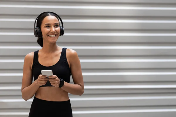 Mulher em roupas esportivas e fones de ouvido sem fio descansando com smartphone depois de treinar ao ar livre — Fotografia de Stock