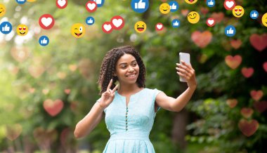 Neşeli bin yıllık siyahi kadın blogcu, parkta blog veya sosyal ağlar için telefonda fotoğraf çekiyor