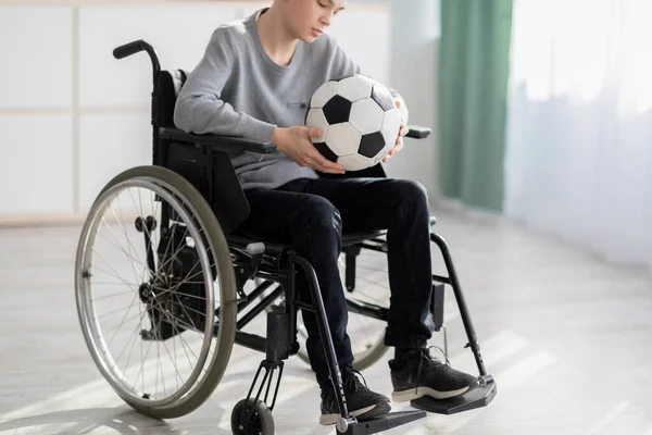 Fogyatékos tini fiú focilabdával ül tolószékben, szenved a sérülése miatt, nem tud otthon játszani. — Stock Fotó