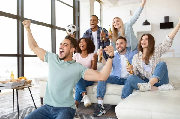 Emotional diverse friends with soccer ball, beer and snacks watching football game on TV at home — Stock Photo, Image