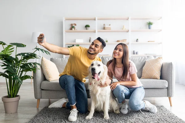 Ευτυχισμένο διαφυλετικό ζευγάρι που παίρνει selfie με το σκύλο τους, ενώ κάθεται σε μαλακό χαλί στο σπίτι, σε όλο το μήκος — Φωτογραφία Αρχείου