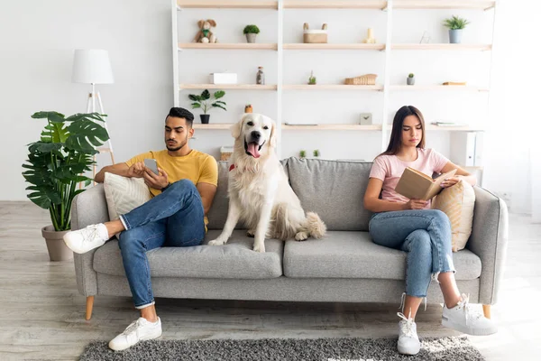 Jeune couple inrerracial ayant un conflit, assis sur les côtés opposés du canapé à la maison, chien de compagnie entre eux — Photo