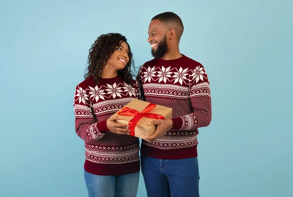 Christmas, new year gifts. Happy black man giving Christmas gift to wife, celebrating xmas together, blue background