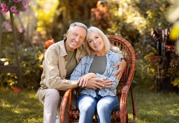 Milující starší manželé odpočívající na venkově, žena sedící v proutěném křesle, muž objímající ženu, kopírovací prostor — Stock fotografie