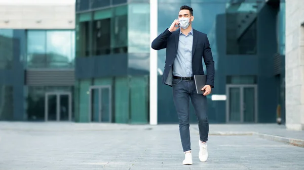 Empresario de Oriente Medio con máscara facial hablando por teléfono mientras camina — Foto de Stock
