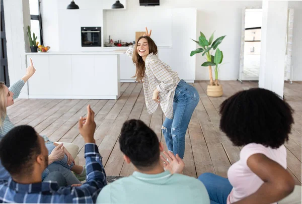 Bonita jovencita mostrando acertijos de pantomima, sus diversos amigos tratando de adivinar durante la fiesta estudiantil en casa — Foto de Stock