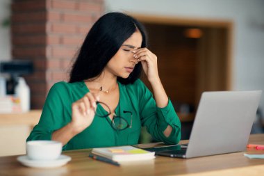 Yorgun Hintli kadın dizüstü bilgisayarın önünde oturuyor.
