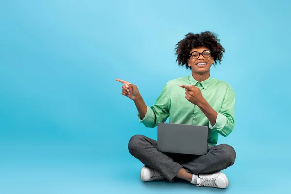 Niezła promocja. Szczęśliwy afrykański nastolatek amerykański facet z laptopem wskazując na wolną przestrzeń nad niebieskim tle — Zdjęcie stockowe