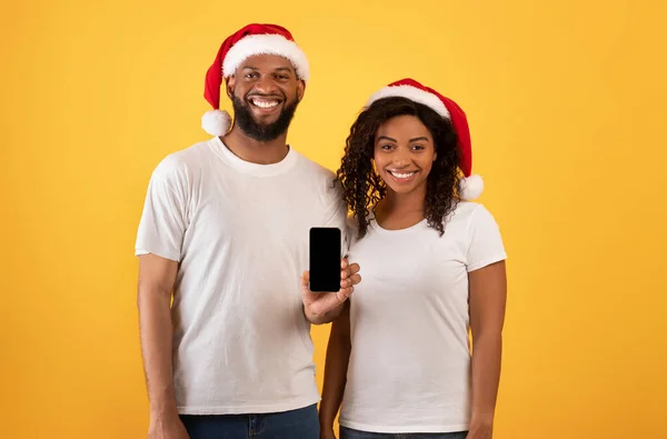 Glada afrikanska amerikanska makar visar smartphone med tom skärm över gul bakgrund, mockup — Stockfoto