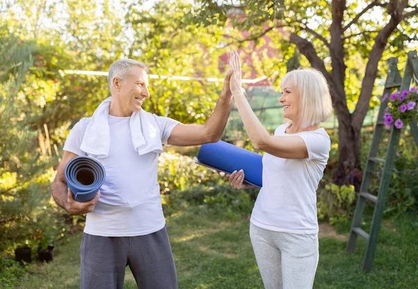 Aktives reifes Paar steht mit Yogamatten und gibt sich nach dem Training im Garten gegenseitig High Five — Stockfoto