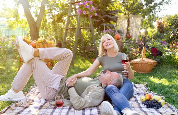 Romantiska äldre makar njuter av picknick tillsammans, vilar på filt i trädgården och dricka rött vin, fritt utrymme — Stockfoto