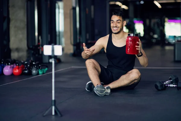 Blogger de fitness árabe bonito gravando revisão de vídeo para nutrição esportiva no ginásio — Fotografia de Stock