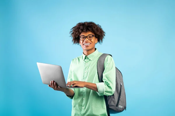 Koncepcja edukacji internetowej. szczęśliwy czarny student facet z plecakiem i laptop komputer, stojąc nad niebieskim tle — Zdjęcie stockowe