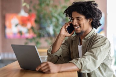 Uzaktan kumanda. Kafede dizüstü bilgisayar ve cep telefonu kullanan genç siyahi serbest çalışan adam.