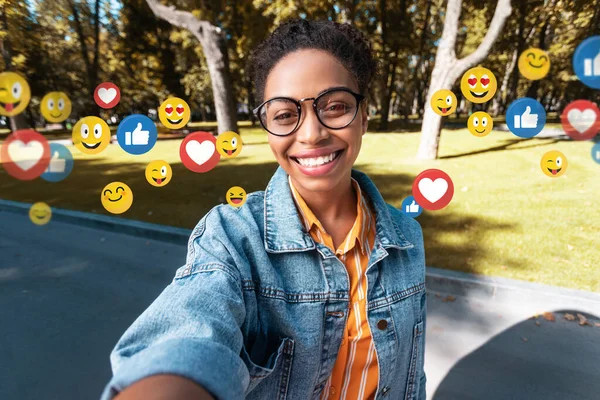 Feliz millennial afro americana dama en casual, gafas hace selfie en parque para redes sociales y blog — Foto de Stock