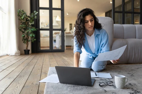 Fokuserad ung kvinnlig frilansare som arbetar på nätet, tittar igenom finansiella dokument, använder laptop inomhus, kopierar utrymme — Stockfoto