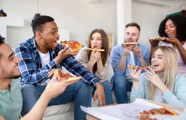 Positieve interraciale vrienden die thuis feest, zitten op de bank, pizza eten, plezier hebben samen binnen — Stockfoto